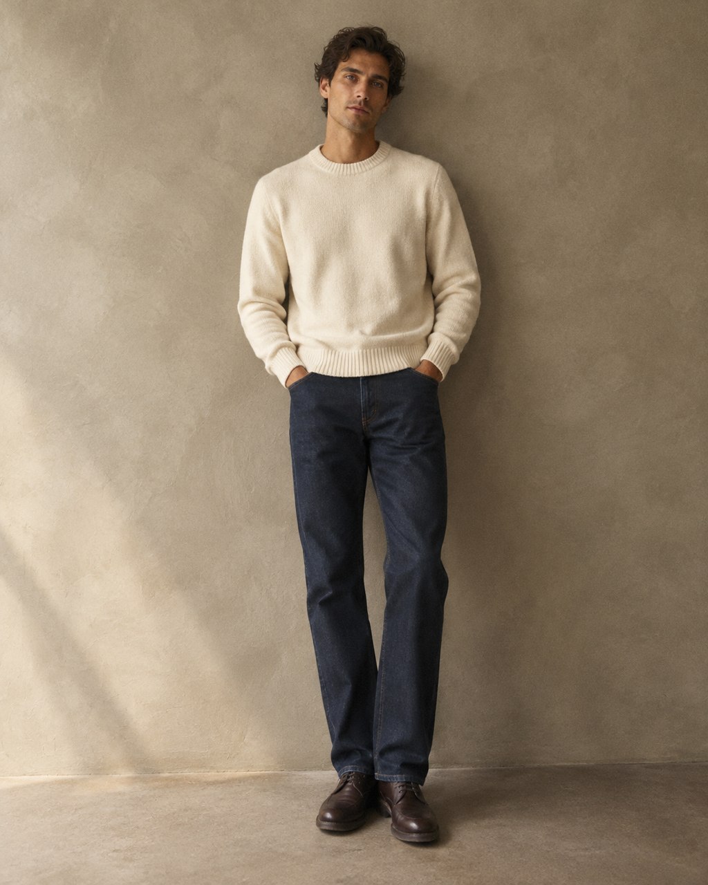 Man wearing dark indigo straight-leg jeans and a cream knit sweater